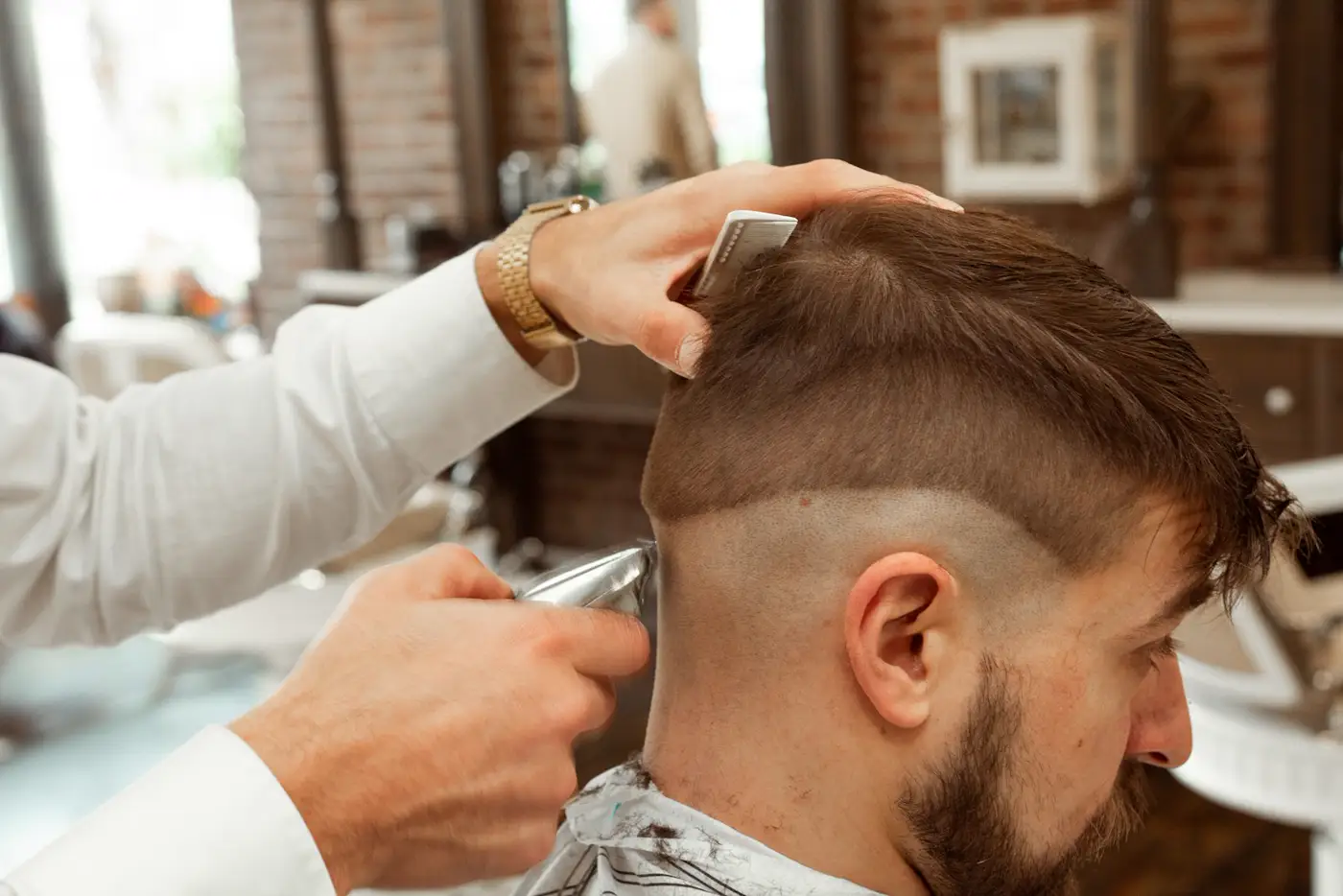 Barbero con camisa blanca cortando el cabello a un cliente en la silla