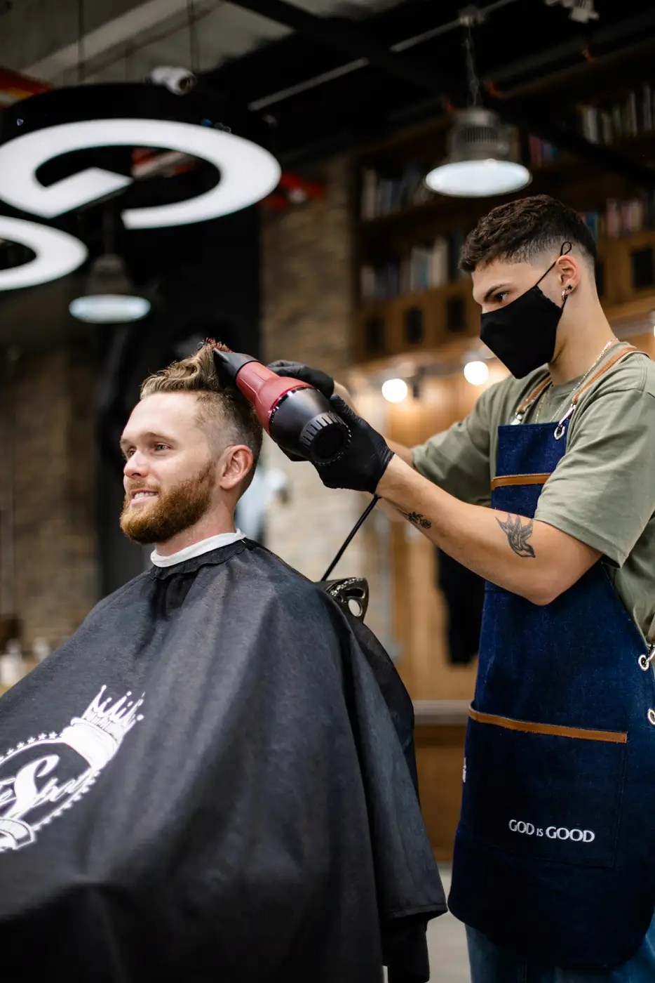 Barbero con delantal de mezclilla secando el cabello de un cliente