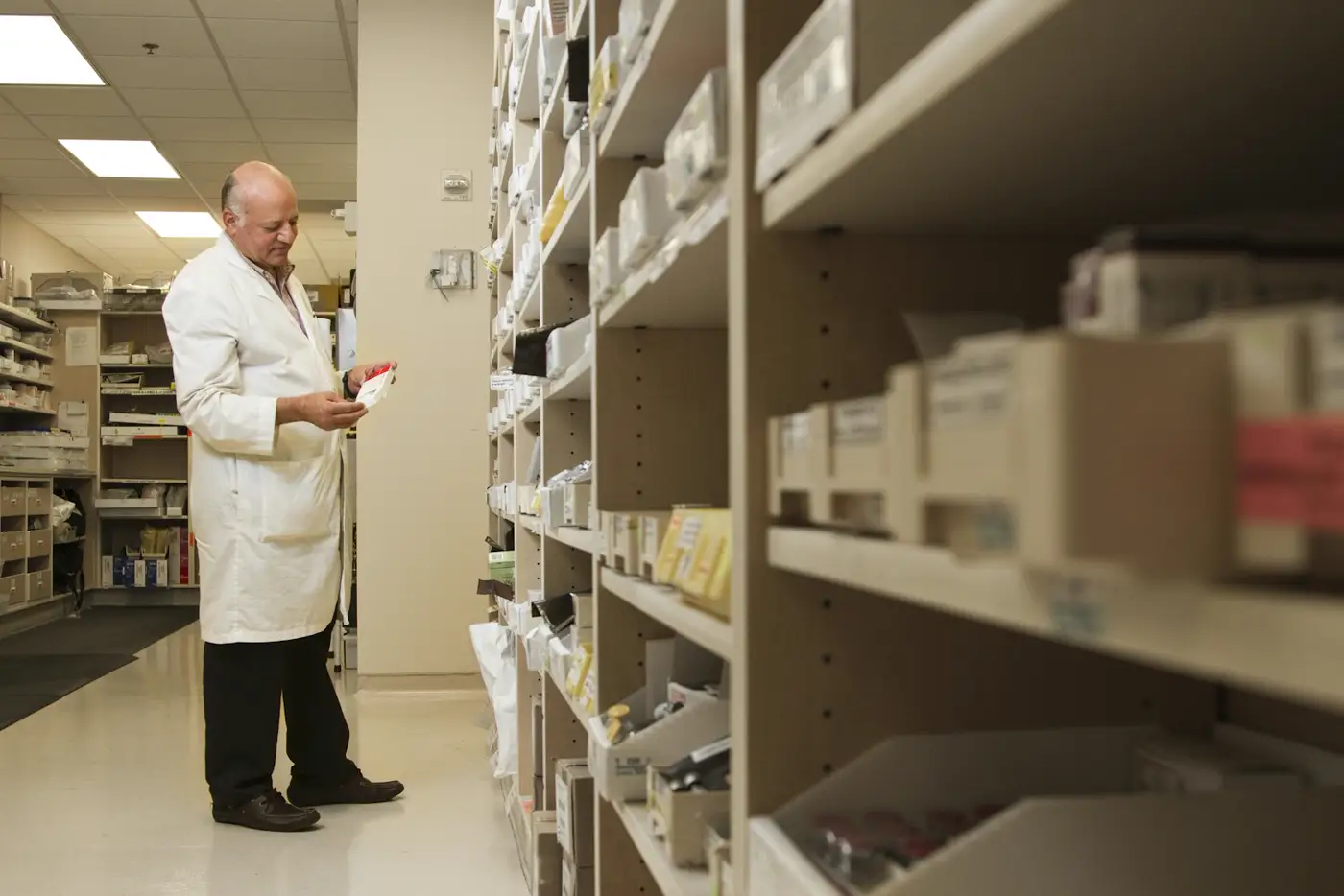 Dependienta de bata blanca atendiendo junto a los estantes de la farmacia